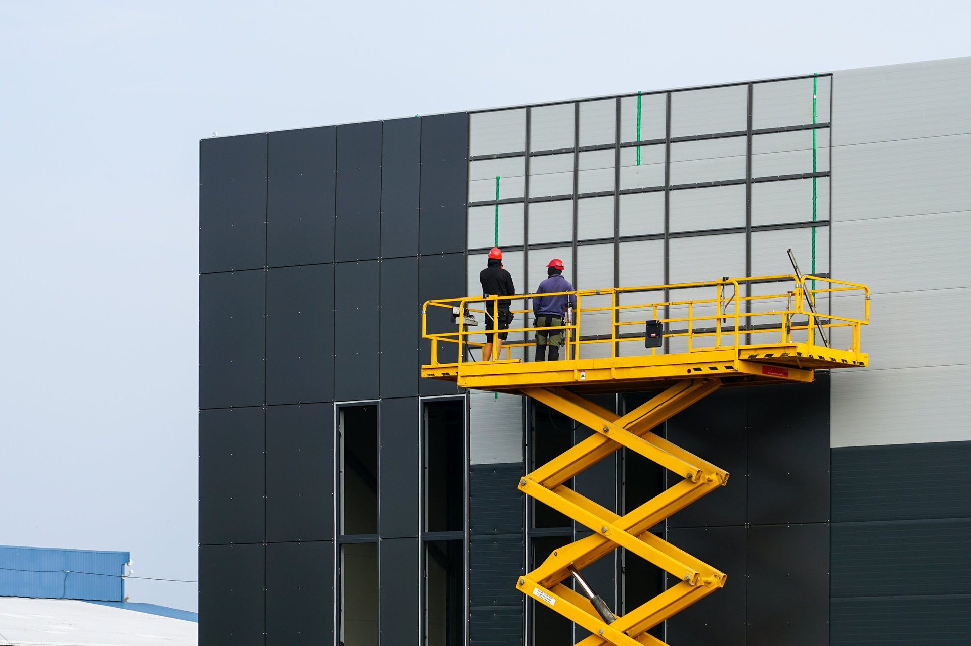 Große gelbe Arbeitsbühne mit Arbeitskräften an einem neuen Industriegebäude